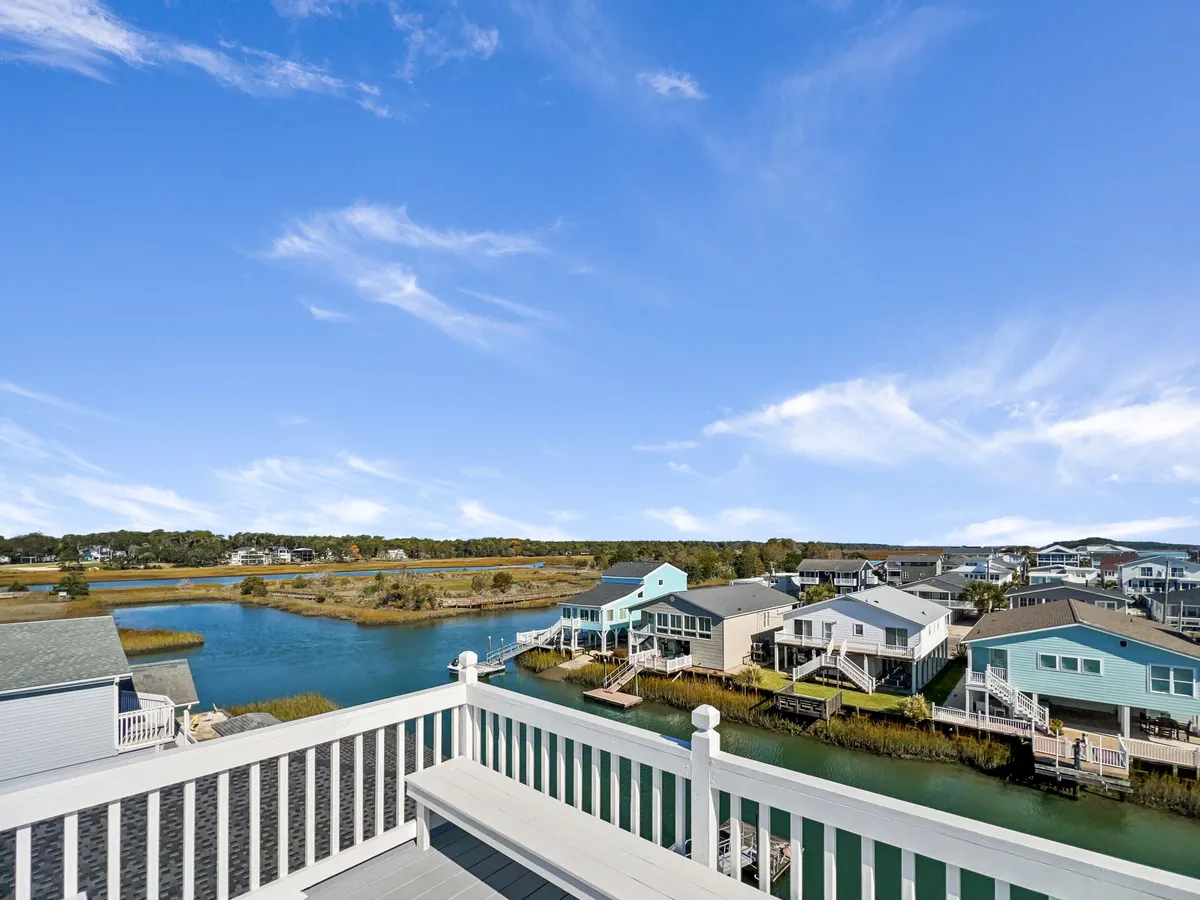 A broad view of a tranquil waterway with colorful houses along the shore and a distant, inviting landscape. The scene is bathed in soft light, ideal for sunset or leisurely evening strolls after sun-filled days at the beach.