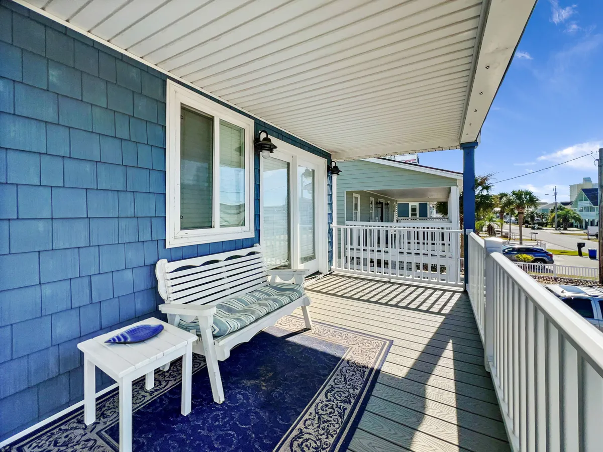 This exterior image shows a charming entryway with blue walls, a decorative rug, and a white bench. The area is functional for relaxing or transitioning after a day at the beach, easily accommodating sandy feet or a quick rest before heading inside. The inviting setup makes it ideal for guests to drop off towels or leash up a pet, reinforcing the home's pet-friendly, seamless indoor-outdoor flow.