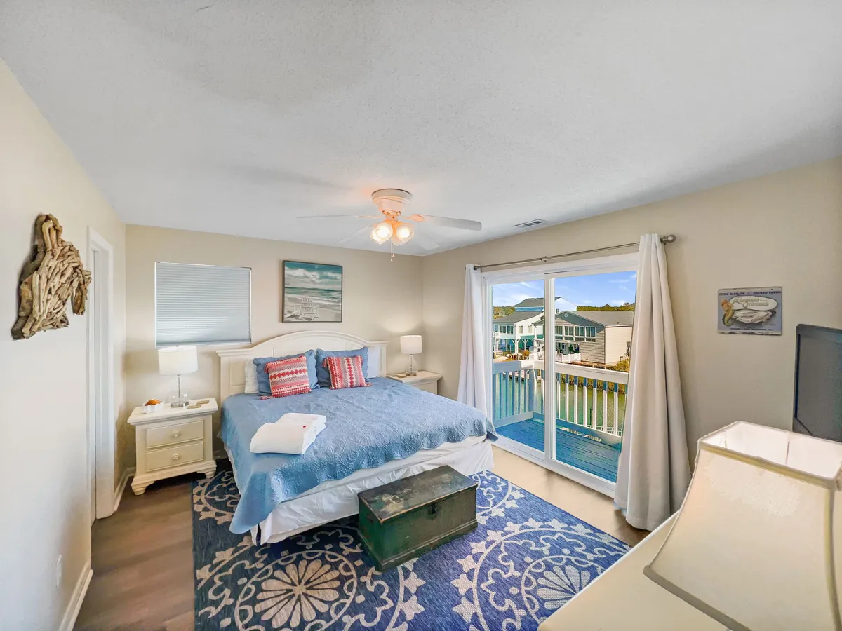 This image displays a serene bedroom featuring a bed with blue bedding, large windows offering an expansive view, and a decorative rug. The room is bathed in natural light, creating a peaceful setting perfect for restful retreats.
