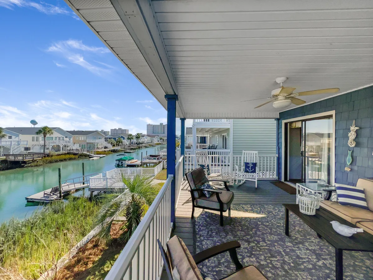 A cozy outdoor seating area overlooks a calm waterway, with decorative elements like an anchor and potted plants adding charm. The porch invites relaxation, and guests can enjoy morning coffee, read, or entertain friends while taking in the tranquil channel views.