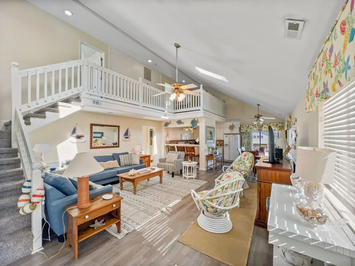 An open and inviting living area with a comfortable sofa, coffee table, rocking chair, and a view of the staircase, all arranged for easy socialization. The space is filled with natural light and decorated in a casual, welcoming style, perfect for gathering with friends or family for conversations, games, or movie nights.