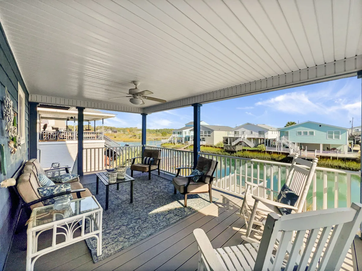 A comfortable outdoor seating area overlooking a scenic water view, featuring a decorative table and plush chairs. The space is perfect for relaxing after a day at the beach or socializing with family and friends while enjoying the breeze and the view.