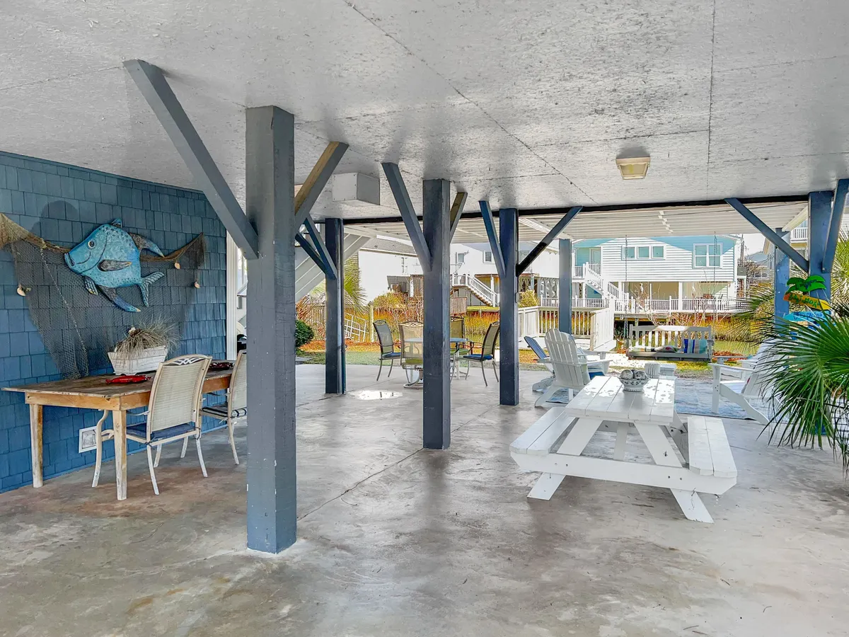 A bright, casual indoor space featuring an outdoor dining table adjacent to a colorful fish mural and lounge chairs. The doors open directly to the outdoors, reinforcing the idea of seamless movement between inside and out. This area is ideal for gathering after beach adventures to dine, relax, and share stories from the day.