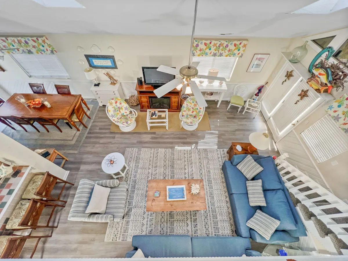 This image presents a cheerful and welcoming open-plan living area, featuring a blue sofa, a wooden coffee table, a dining table with colorful chairs, and decorative wall art. The room exudes warmth and is clearly set up for both relaxation and group gatherings, with sightlines connecting the living and dining spaces.